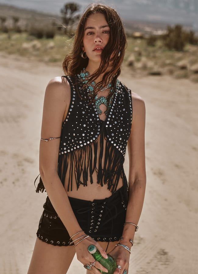 model in desert wearing Bohemian Music Festival black suede, tasselled and studded vest and shorts