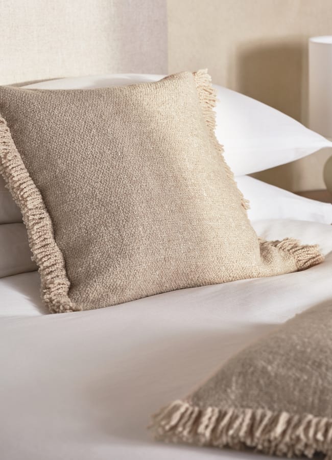 beige textured and fringed cushions on white bedding
