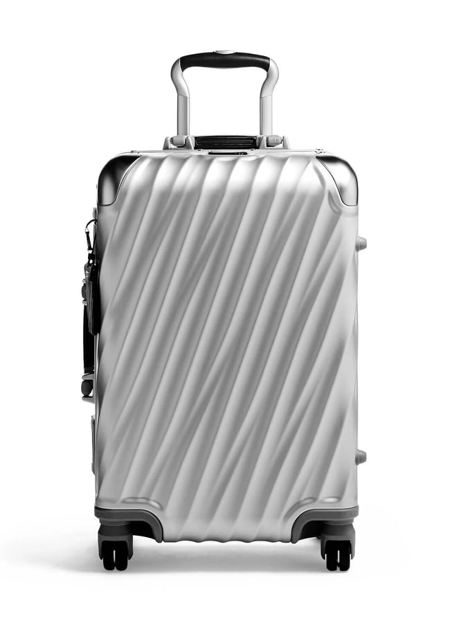 A silver hard-shell suitcase from one of the best suitcase brands, featuring diagonal ridges, four black wheels, a retractable handle, and reinforced metal corners, shown standing upright on a white background.