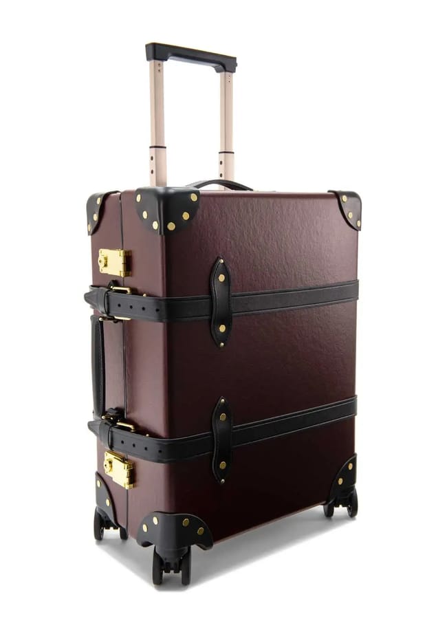 A vintage-style hard-shell suitcase in dark brown with black straps, gold metal accents, and an extended telescopic handle—designed to rival the best suitcase brands. Features four wheels for easy rolling.