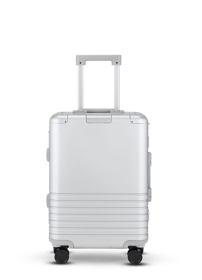 A silver hard-shell cabin suitcase from one of the best suitcase brands, featuring a telescopic handle and four black wheels, is shown standing upright against a white background.