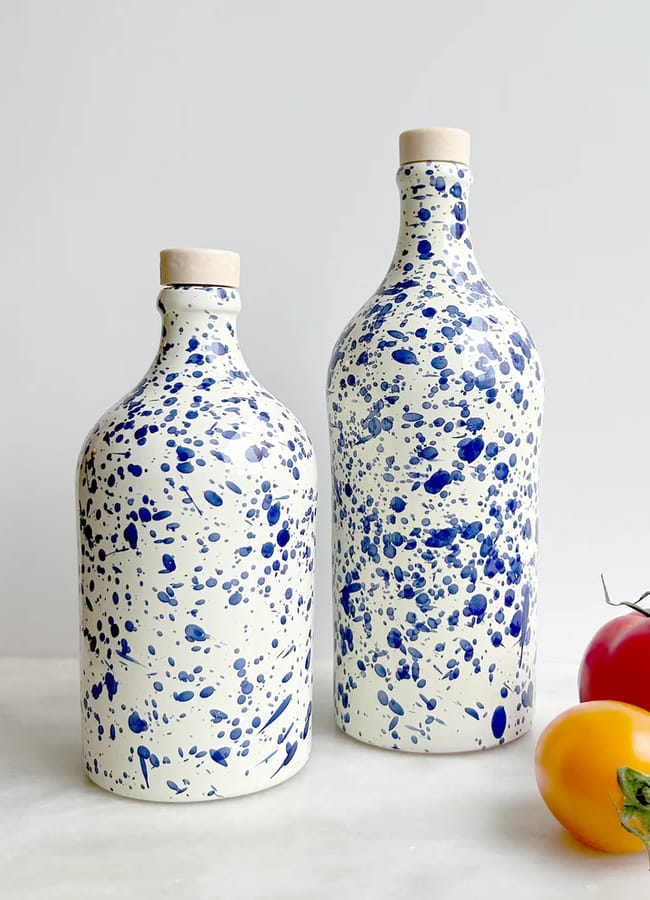 Two ceramic bottles with cork stoppers, decorated with blue splatter patterns on a white background, stand beside red and yellow tomatoes on a white surface.