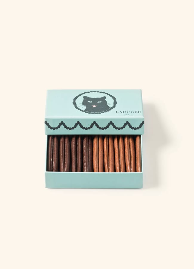 A light blue Ladurée box with a black cat illustration on the lid, opened to show two neat rows of assorted chocolate-covered biscuits inside—an elegant choice for Father’s Day gifts 2026.