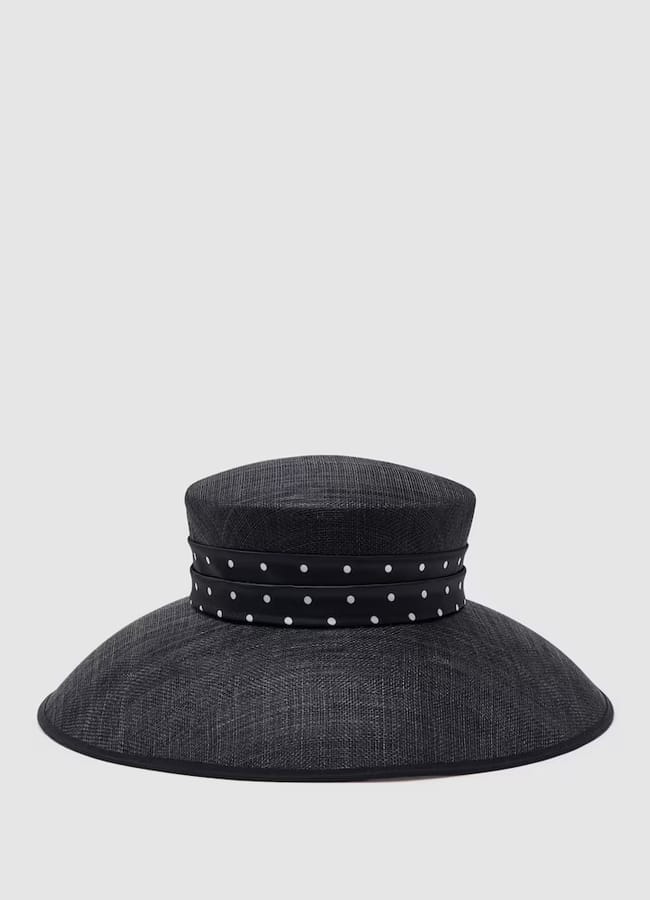 Wide-brimmed black hat with a flat crown, featuring a black band decorated with white polka dots—a classic look that makes a strong case to ban fascinators, set against a plain light grey background.
