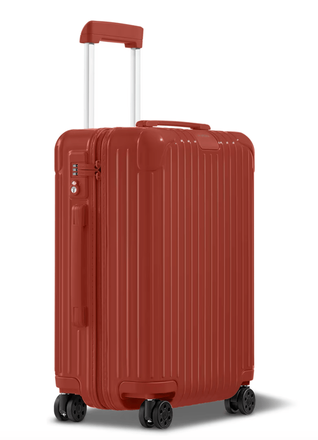 A red hard-shell suitcase from one of the best suitcase brands, featuring four wheels, a telescopic handle, and vertical ridges, stands upright against a plain white background.