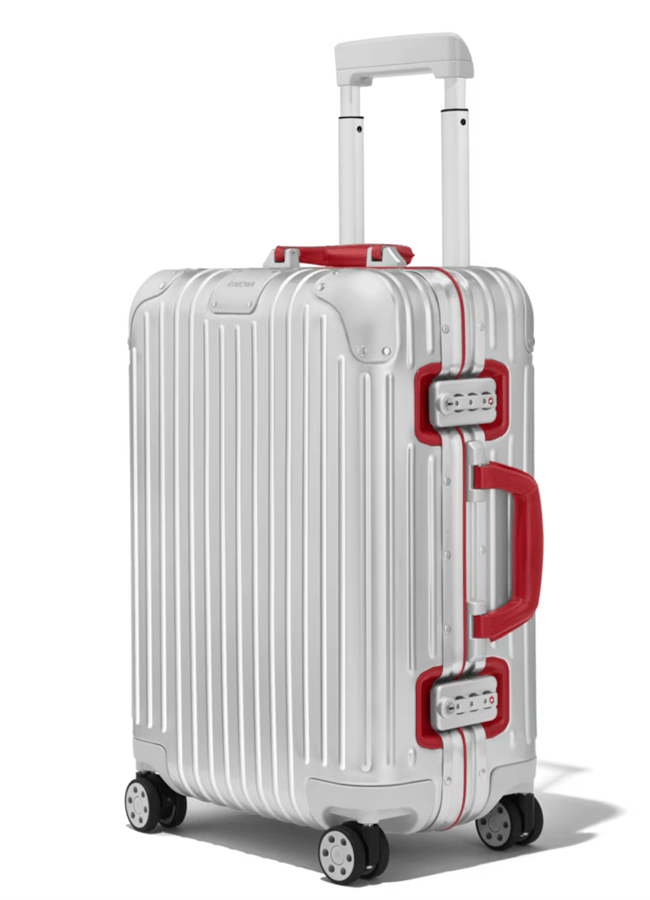 A white hard-shell suitcase with vertical ridges, red handles, red corner accents, and four black swivel wheels—an eye-catching piece inspired by the best suitcase brands—stands upright on a white background.