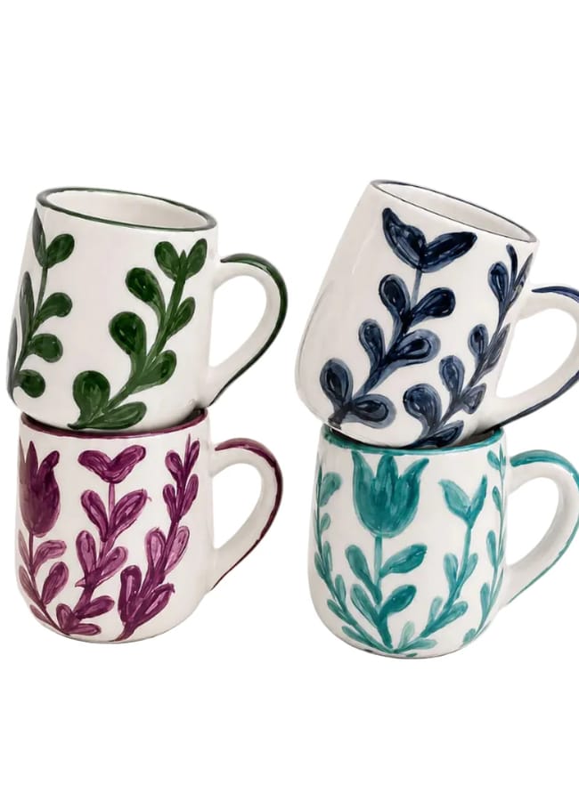 Four ceramic mugs with painted leaf designs in green, blue, purple, and teal, stacked in pairs with one mug on top of another against a white background.