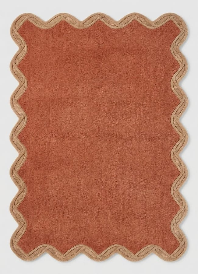 A rectangular rust-coloured rug with wavy, scalloped tan edges, displayed on a white background—perfect for adding a touch of maximalist hotels-inspired flair to any space.