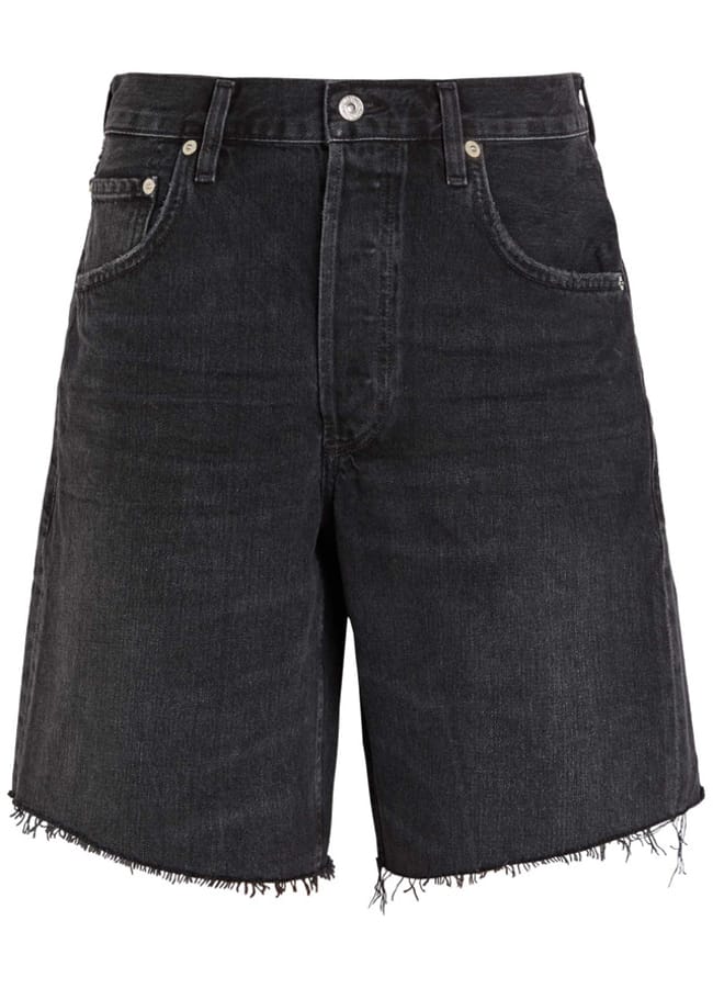 These black denim shorts, a must-have among the best denim shorts, feature raw frayed hems, five pockets, silver rivets, and a button zip fly with a slightly faded, worn look.