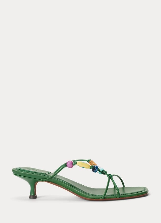 A green heeled sandal with a thin strap adorned with colourful beads, featuring a low kitten heel and an open toe design—perfect for what to wear in Ibiza, shown on a white background.