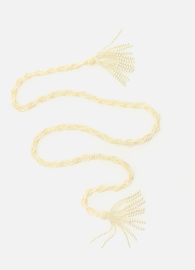 A long, twisted pearl necklace with tassels at both ends, laid out in a zigzag pattern on a plain white background—a statement piece inspired by high street fashion.