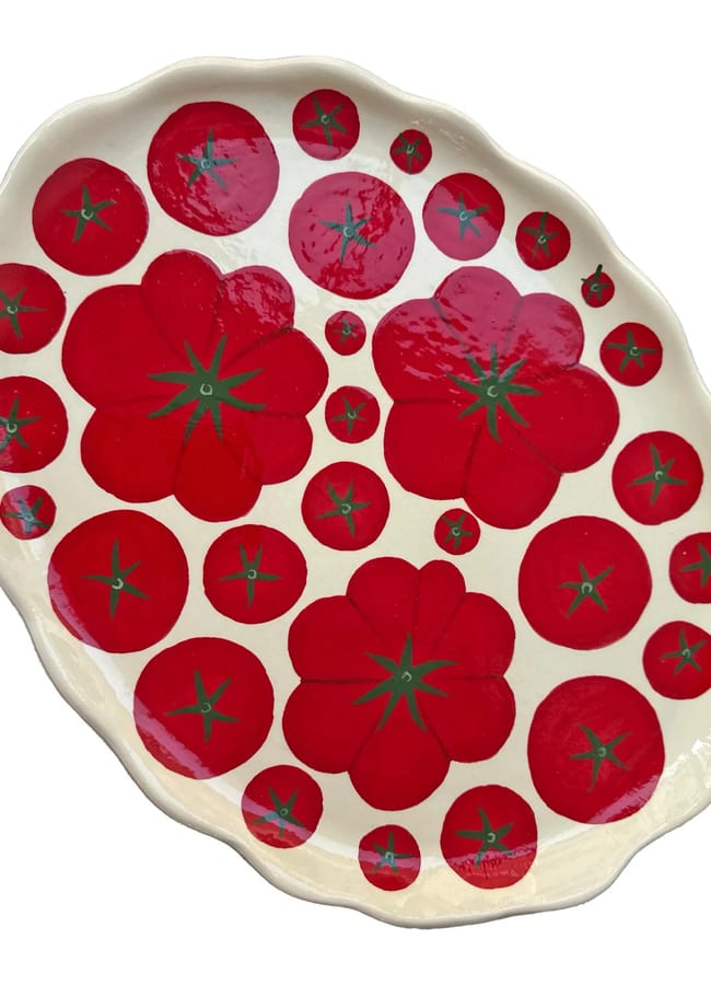 An oval ceramic plate with a wavy edge, decorated with vibrant red tomato designs of various sizes and green stalks on a white background—perfect for brightening up your table during salad season.