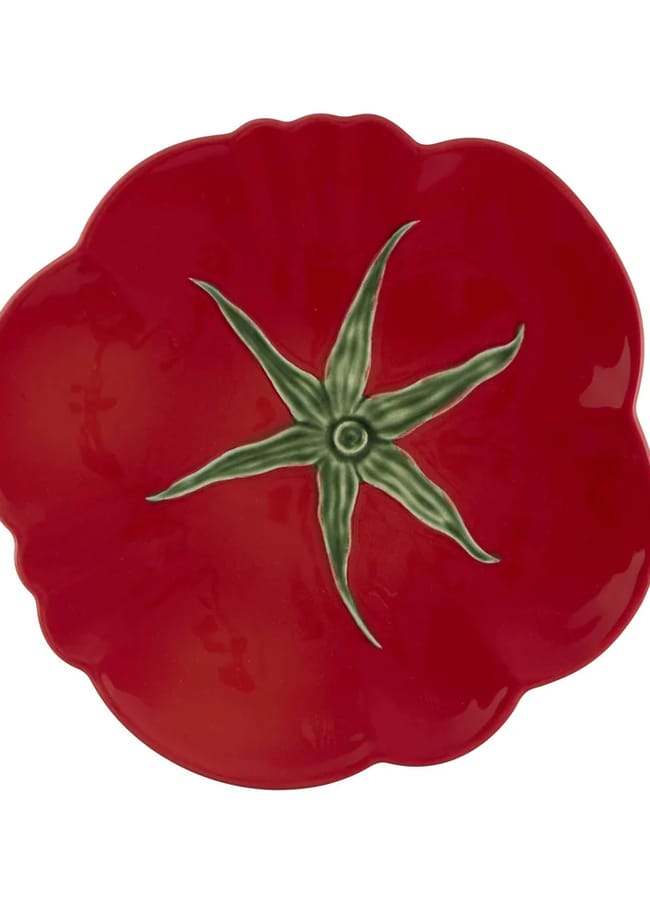 A ceramic plate shaped and painted like a red tomato with a green stalk design in the centre, perfect for serving during salad season, viewed from above on a white background.