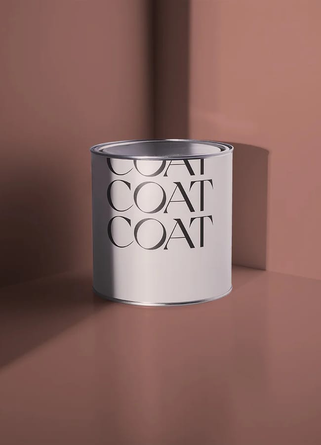 A silver paint tin with a white label showing the word COAT repeated three times, set against a pinkish-brown background with angular shadows—an aesthetic that wouldn’t look out of place in the bold interiors of maximalist hotels.