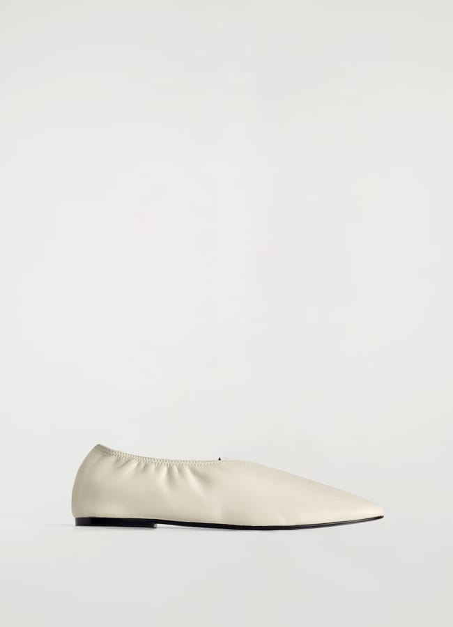 A minimalist, cream-coloured flat shoe with a pointed toe and elasticated top—perfect for elevating any high street fashion look—shown in profile against a plain white background.
