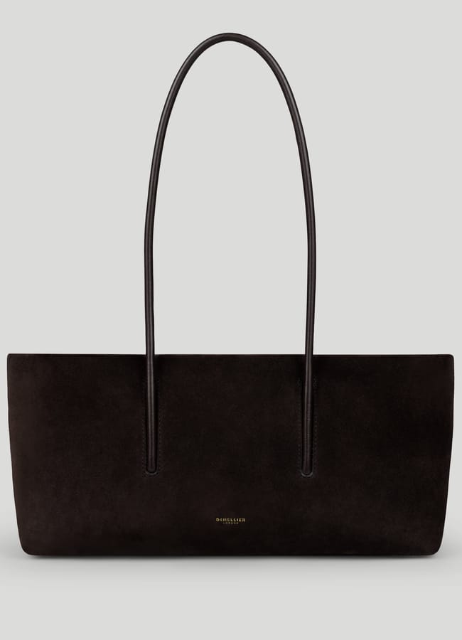 A black suede tote bag with two long, thin handles and a minimalist design, this high-end designer bag features small gold text near the bottom centre. The background is light grey.