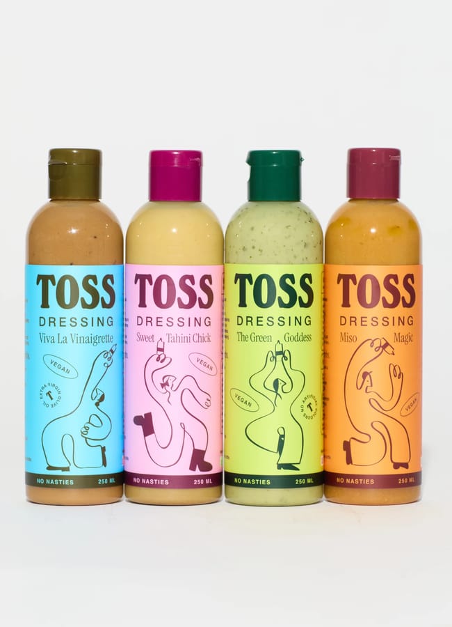 Four colourful bottles of TOSS Dressing are lined up, perfect for salad season. Each unique label and flavour—Viva La Vinaigrette, Sweet Tahini Chick, The Green Goddess, and Miso Magic—features playful abstract art.