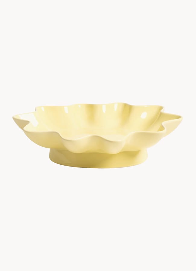 A pale yellow ceramic bowl with a glossy finish and a wavy, scalloped edge sits on a round base—perfect for brightening up salad season—against a plain white background.