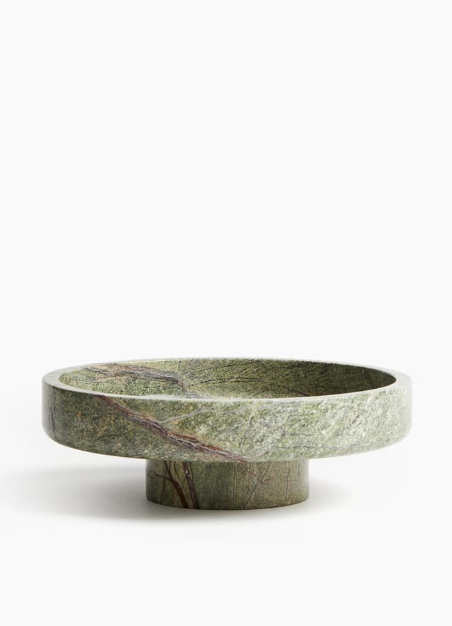 A round, shallow green stone bowl with subtle natural patterns, elevated on a short cylindrical base—perfect for salad season—set against a plain white background.