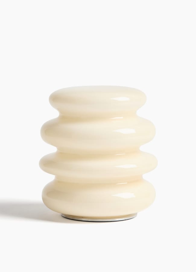 A cream-coloured, glossy, ceramic vase with a rounded, ribbed design featuring four horizontal ridges, reminiscent of the sculptural decor often seen in maximalist hotels, set against a plain white background.