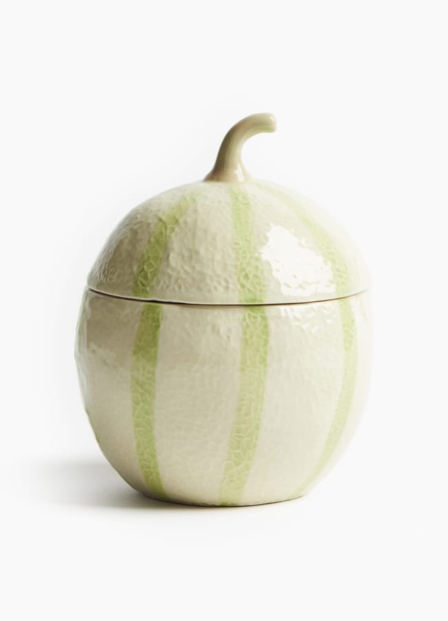 A ceramic container shaped like a melon with light green vertical stripes and a curved stem on top, set against a white background—perfect for adding whimsical charm to your foodie homewares collection.