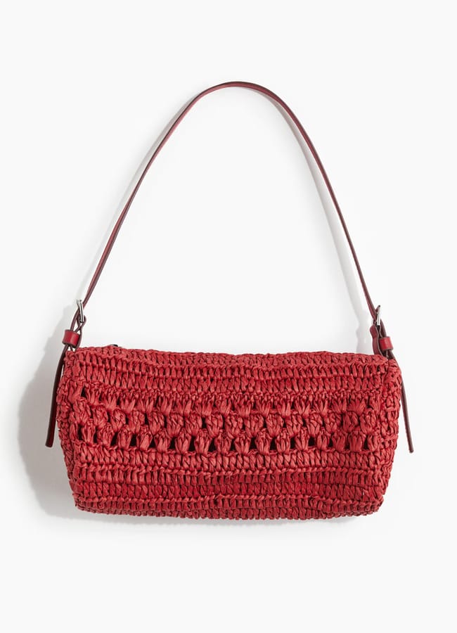 A red, rectangular, handwoven crochet shoulder bag with a single thin strap and a textured pattern—perfect for completing your look when deciding what to wear in Ibiza—displayed on a white background.