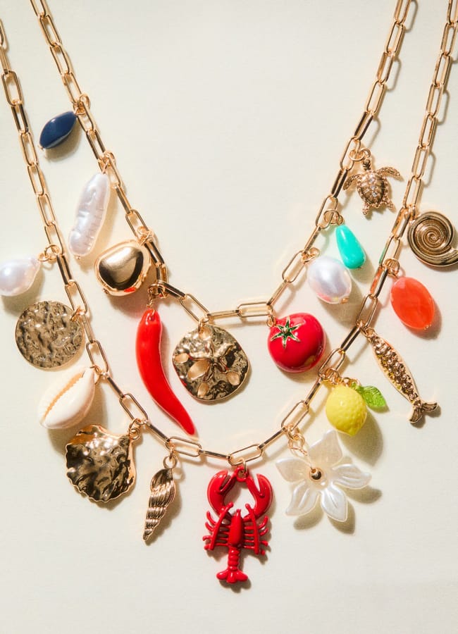 Three gold chain necklaces decorated with assorted charms, including seashells, a lobster, a chilli pepper, a tomato, a lemon, pearls, and various gold and colourful beads—all arranged on a neutral background—make for vibrant colourful jewellery that adds playful flair to your collection of unique jewellery pieces.