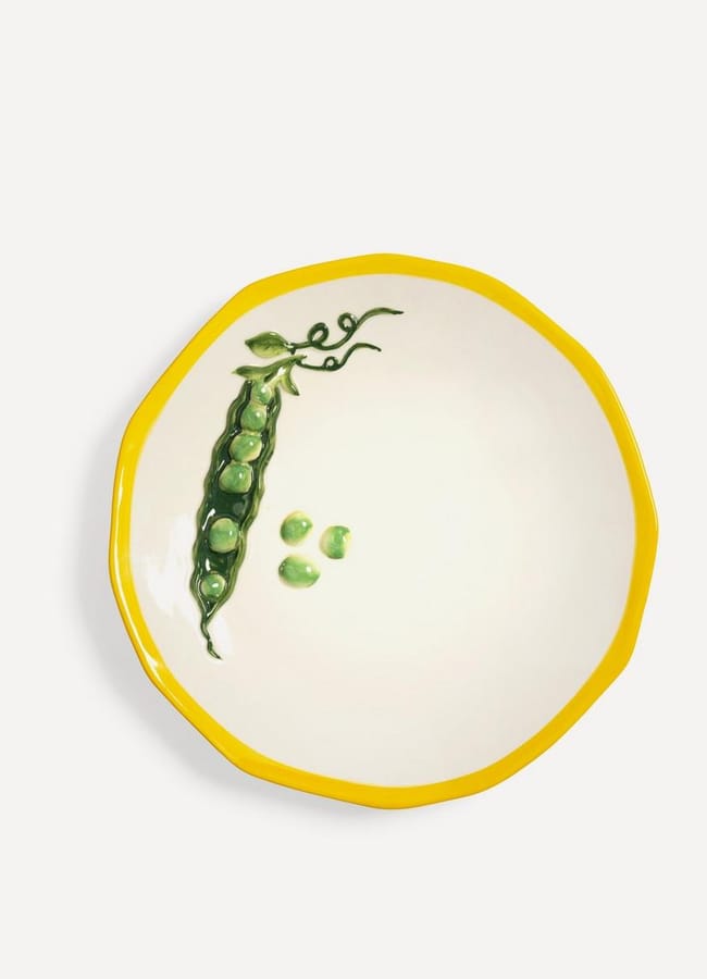 A round white plate with a yellow rim, featuring a painted green pea pod and three loose peas on one side—an ideal choice for the discerning foodie seeking unique homewares.