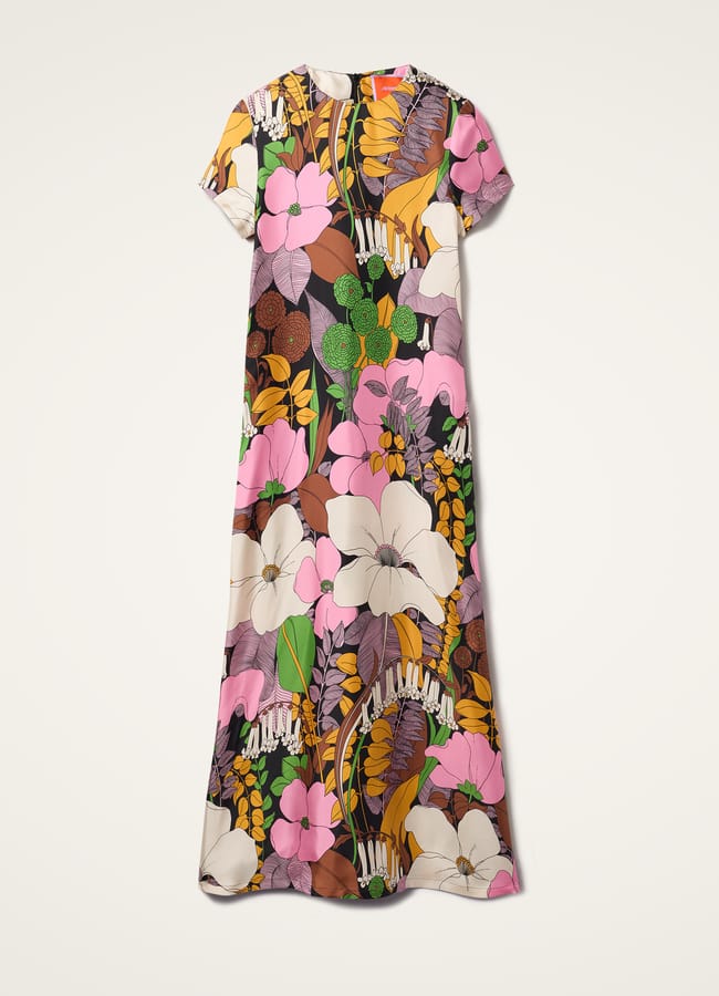 Short-sleeve, ankle-length dress featuring a bold, colourful floral print with large pink, white and yellow flowers and green leaves on a black and brown background, laid flat on a white surface—perfect for anyone wondering what to wear in Ibiza for effortless style.