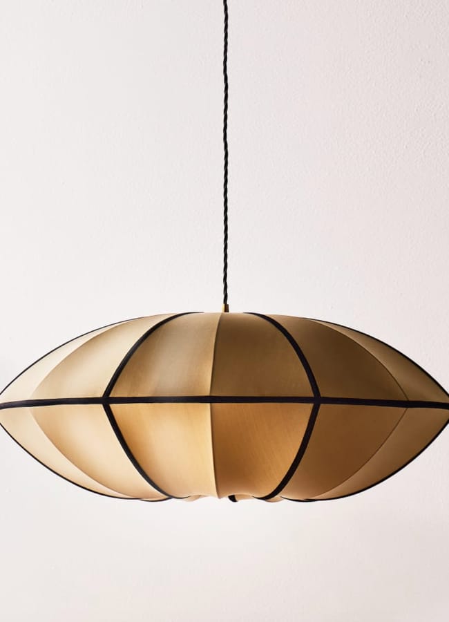 A pendant light with a gold, oval-shaped shade featuring black ribbed segments, hanging from a twisted black flex against a plain white background—perfect for adding a touch of bold sophistication reminiscent of maximalist hotels.