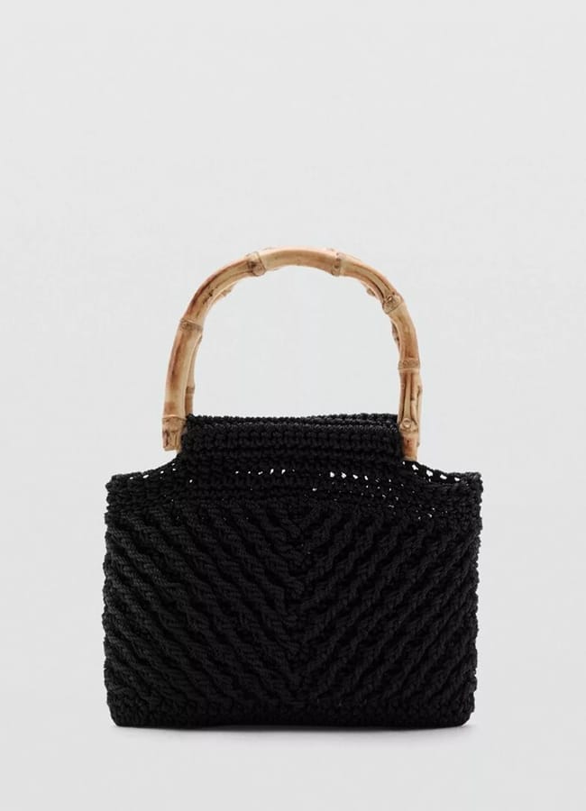 Black woven handbag with a chevron pattern and two curved bamboo handles, displayed against a plain light grey background—a chic accessory perfect for those wondering what to wear in Ibiza.