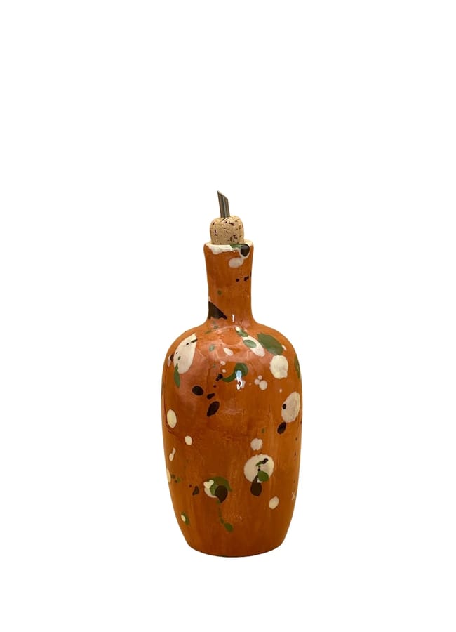 A small, orange ceramic bottle with a round body, narrow neck, and cork stopper. Perfect for salad season, its surface features green, black, and white paint splatters that give it a rustic, artistic appearance.