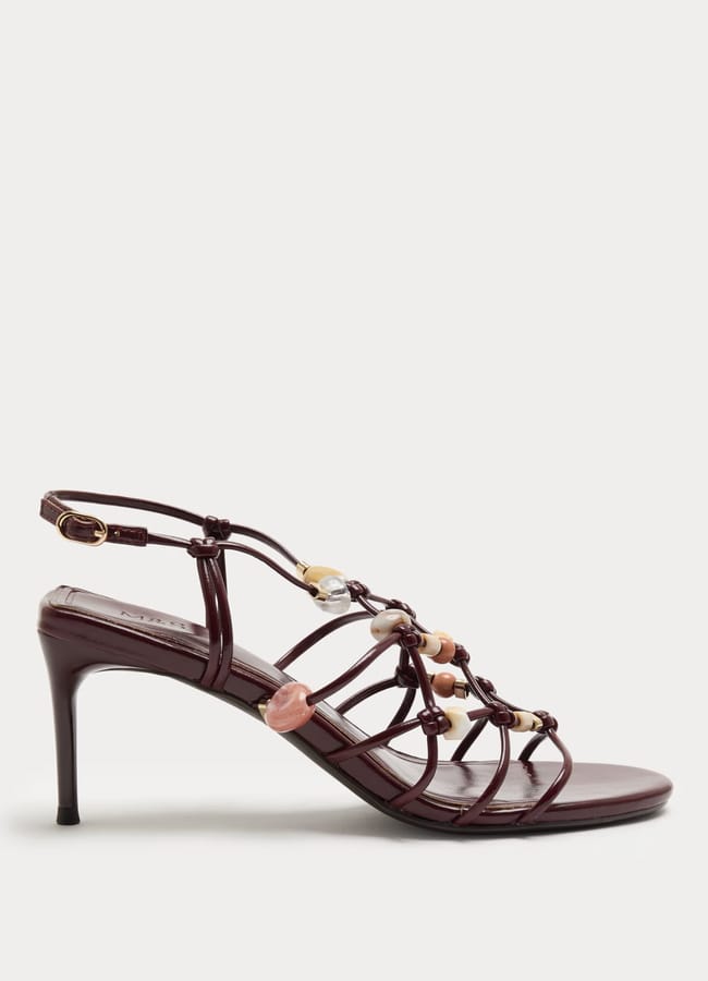 A burgundy strappy high-heel sandal with a slim heel, ankle strap, and decorative multicoloured beads along the upper straps, displayed on a plain white background—perfect for adding a touch of high street fashion to your outfit.