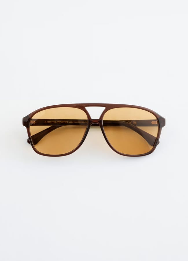 Brown-framed aviator sunglasses with amber lenses, displayed on a plain white background—an essential accessory for any high street fashion look.