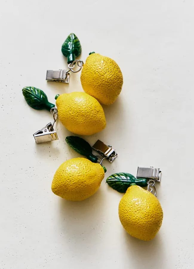 Four realistic lemon-shaped fridge magnets with attached green leaves and metal clips are arranged on a white background—a charming addition to your kitchen accessories collection and a perfect choice for anyone seeking creative cooking gifts.
