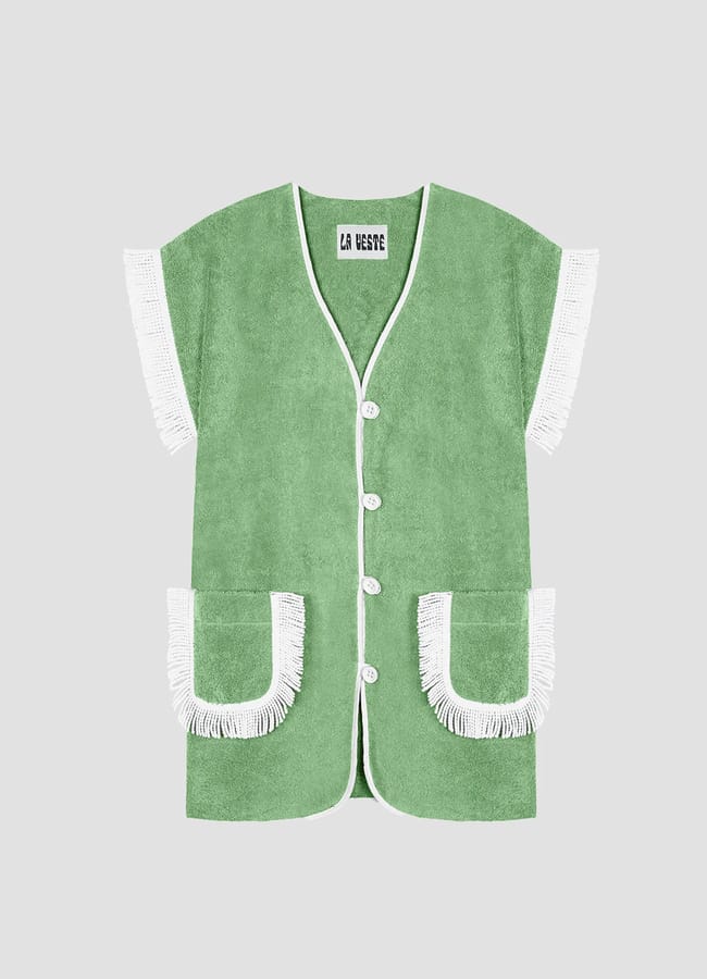 A green short-sleeved waistcoat with white trim, buttons, and fringe details on the sleeves and pockets, displayed on a plain grey background—an effortlessly chic choice for what to wear in Ibiza.