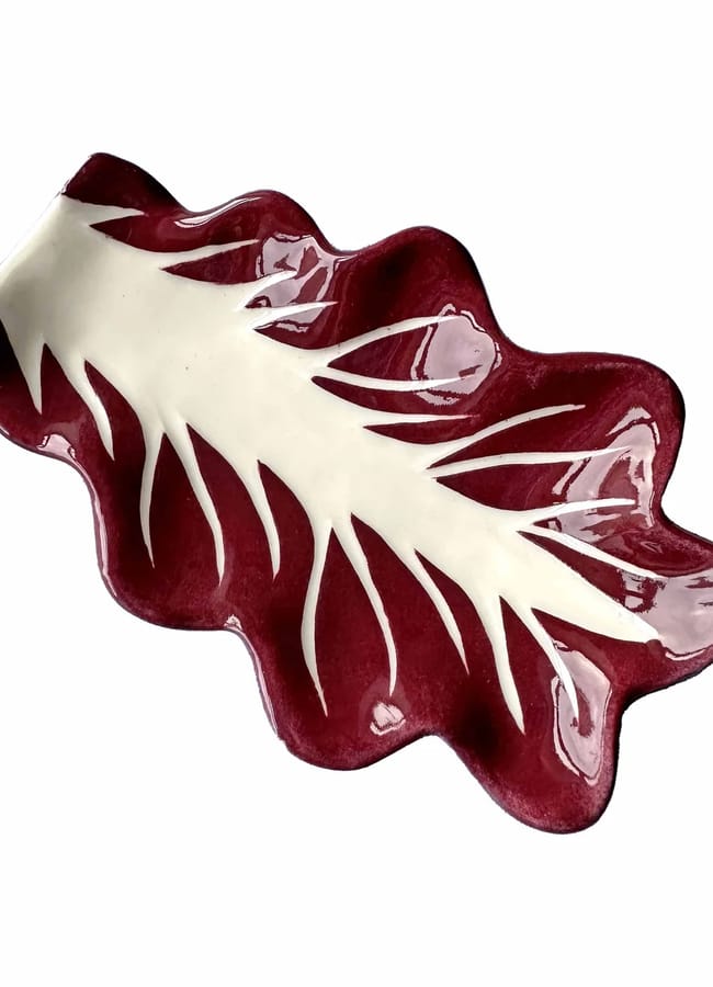 A ceramic dish shaped like a leaf, perfect for salad season, featuring deep red edges and a white centre with vein-like patterns, set against a white background.