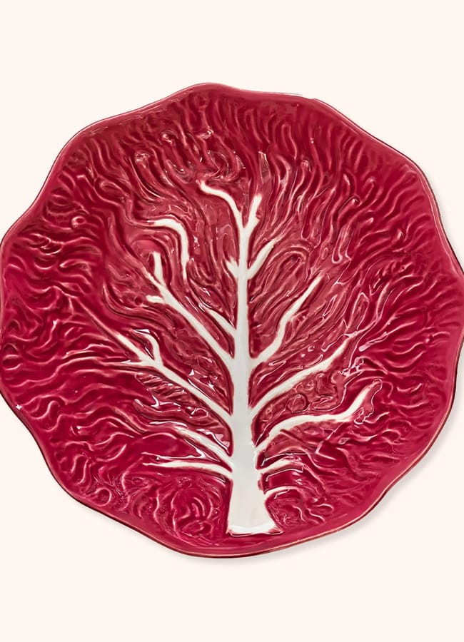A red ceramic plate shaped and textured like a leaf, with raised vein patterns and a white tree-like design in the centre—perfect for serving fresh dishes during salad season.