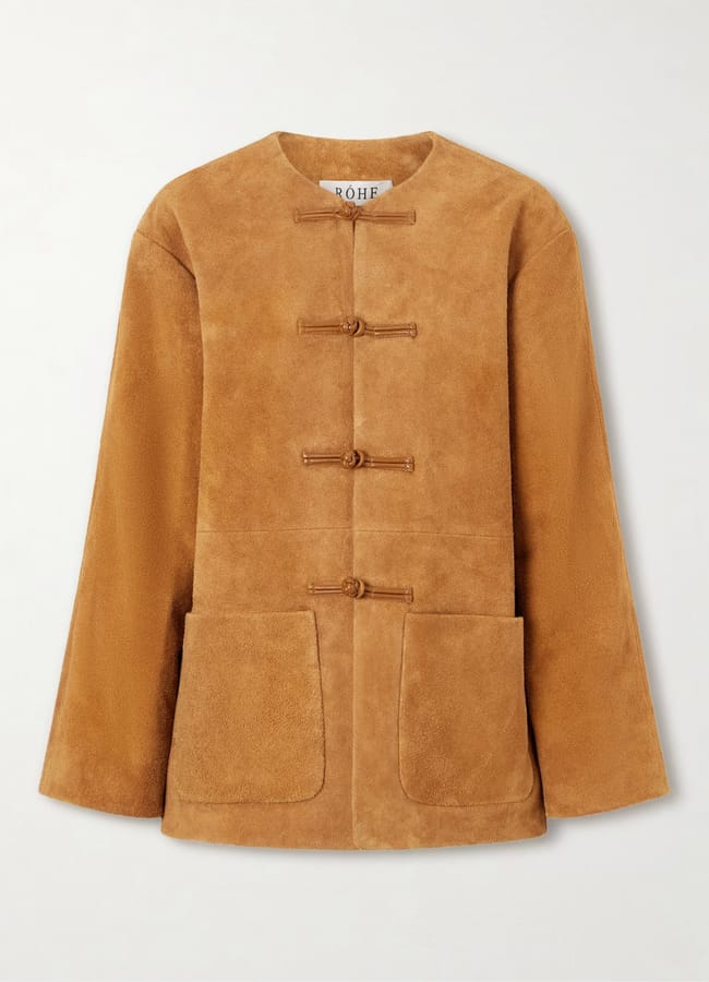 Light brown suede jacket with long sleeves, two large front pockets, and three toggle fastenings down the front. The label inside reads RÓHE. The design is minimal, with no collar and a straight hem, making it a chic outfit choice that highlights every subtle fashion detail.
