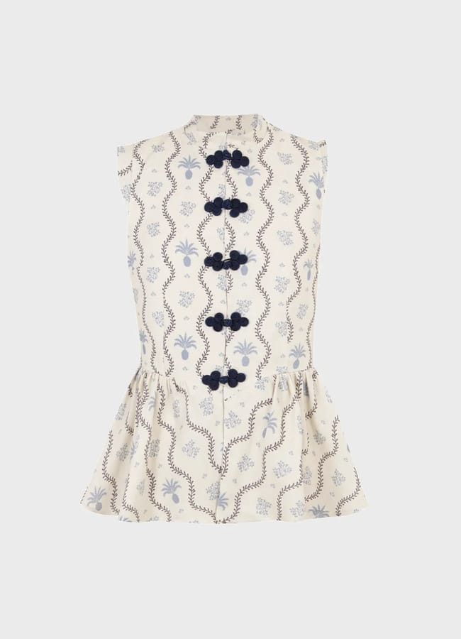 Sleeveless cream blouse with light blue and brown wavy and floral patterns, featuring five navy blue knotted buttons down the front and a frilled peplum hem—an ideal fashion detail to complete any chic outfit.