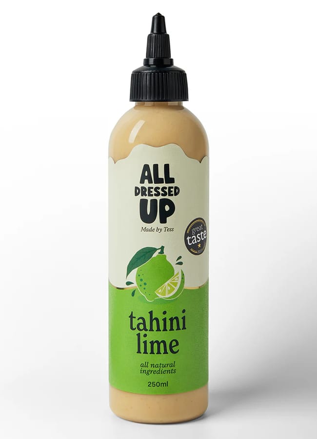 A plastic squeezy bottle labelled ALL DRESSED UP tahini lime, perfect for salad season, features a lime and leaves illustration on a green background. The 250ml sauce bottle has a black twist cap.