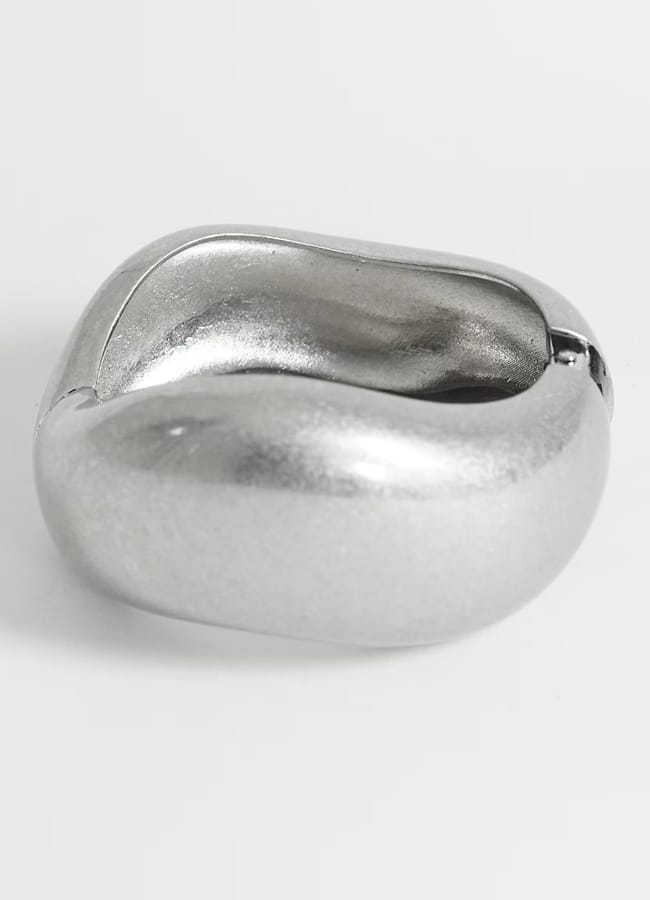 A chunky, smooth, silver ring with a slightly irregular, organic shape on a plain white background—an effortlessly stylish accessory that captures the free-spirited vibe of what to wear in Ibiza.