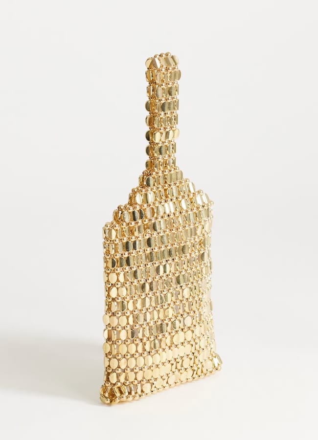 A small clutch bag shaped like a bottle, covered in shiny gold beads, stands upright against a plain white background—an eye-catching piece perfect for adding a touch of high street fashion to any outfit.