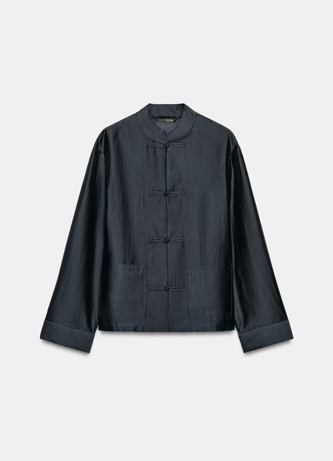 A dark, long-sleeved traditional Chinese jacket with a mandarin collar and frog button fastenings, laid flat on a plain, light background—showcasing unique fashion details perfect for chic outfits.