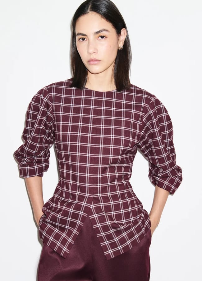 A person with straight dark hair wears a maroon and white checked top with puffed sleeves and maroon trousers, standing against a plain white background—a look that perfectly embodies autumn winter 2026 fashion trends.