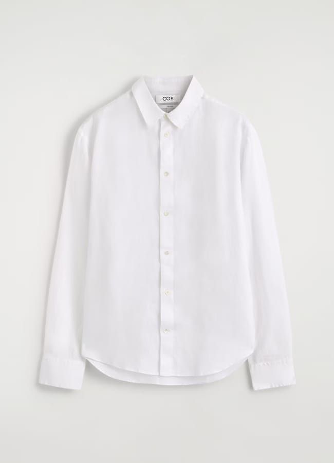 A white, long-sleeve button-up shirt with a collar and cuffs, displayed on a plain light background. The shirt features a straight cut and a subtle COS label on the inside of the collar—an essential piece for men’s fashion and perfect for channelling The Talented Mr Ripley style in your summer wardrobe.