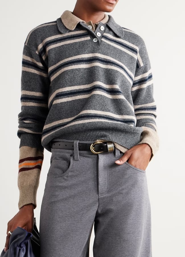 Person wearing a grey and beige striped long-sleeve polo jumper, grey trousers, and a black belt with a gold buckle, holding a dark-coloured bag, with one hand in their pocket—perfect for stepping out in style during our summer sale.