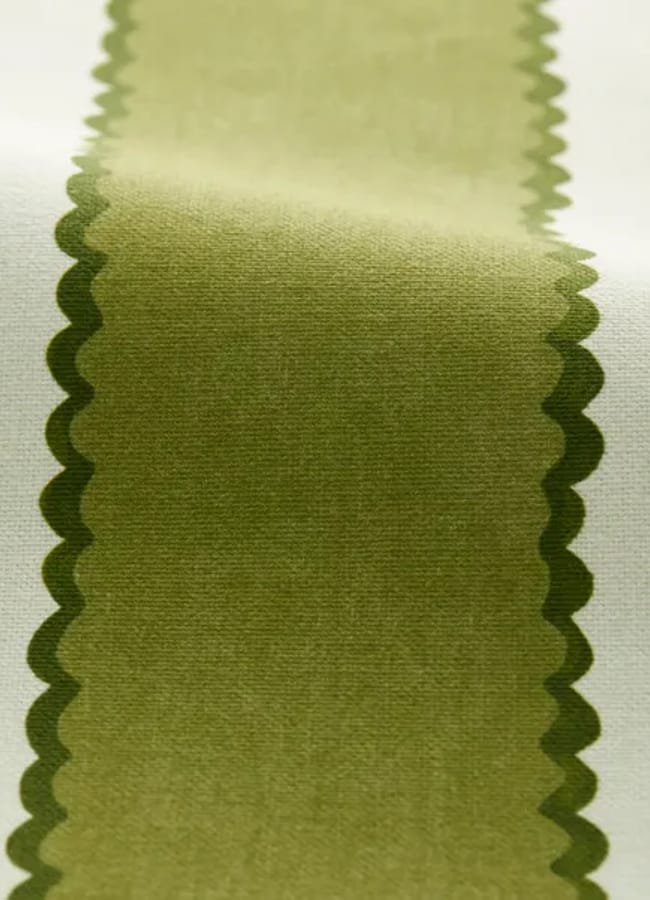 A close-up of fabric with a wide, vertical olive green stripe—evocative of the chartreuse colour trend—bordered by scalloped edges on a white background.