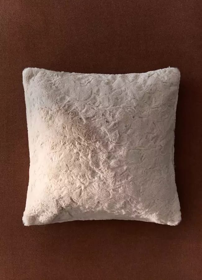A square, cream-coloured, textured cushion is placed on a solid brown surface, seen from above—perfect for creating a cosy spot during an outdoor film night at home.