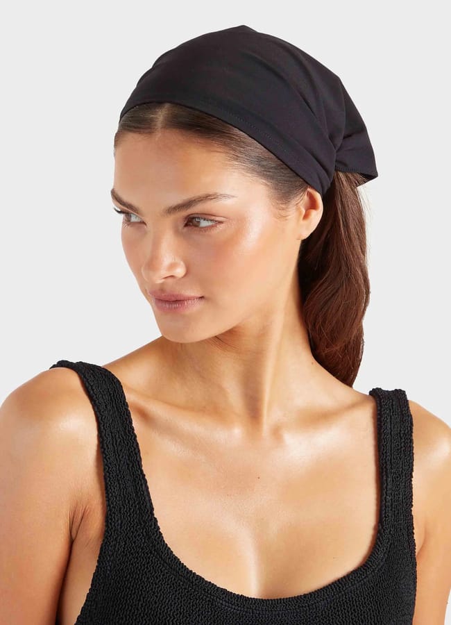 Woman wearing a textured black vest top and a black headscarf, looking to the side with a neutral expression against a plain, light background—an effortless example of minimalist summer fashion.